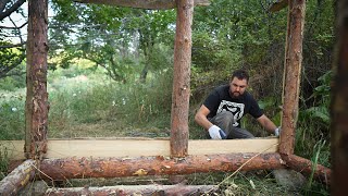 A man builds a wooden house in nature. Cooking over a campfire